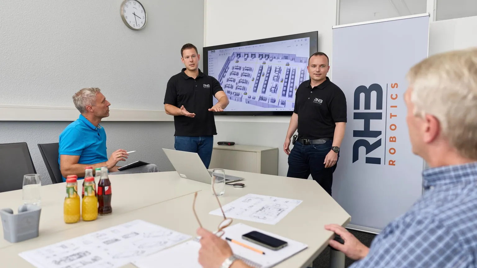Vorstellung eines Hallenlayouts im Besprechungsraum, zwei Mitarbeiter erläutern die geplanten Materialflussstrecken